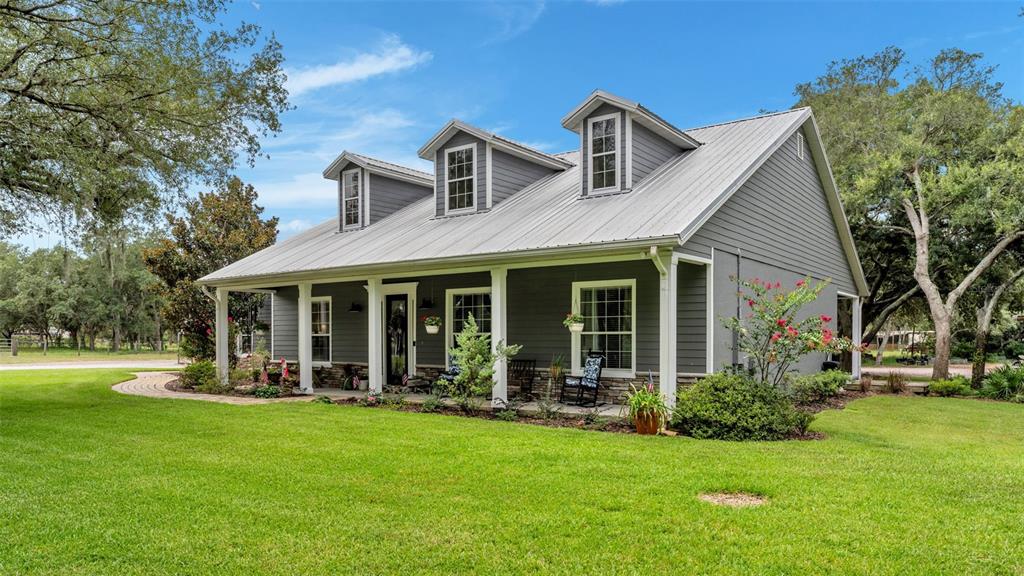 A gray house with a metal roof and three dormers sits on a green lawn — 8044 LAKE HATCHINEHA ROAD, HAINES CITY, FL