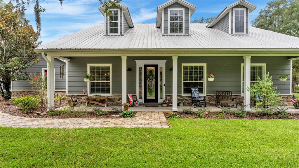 A gray house with a metal roof, dormer windows, and a stone-accented front porch — 8044 LAKE HATCHINEHA ROAD, HAINES CITY, FL