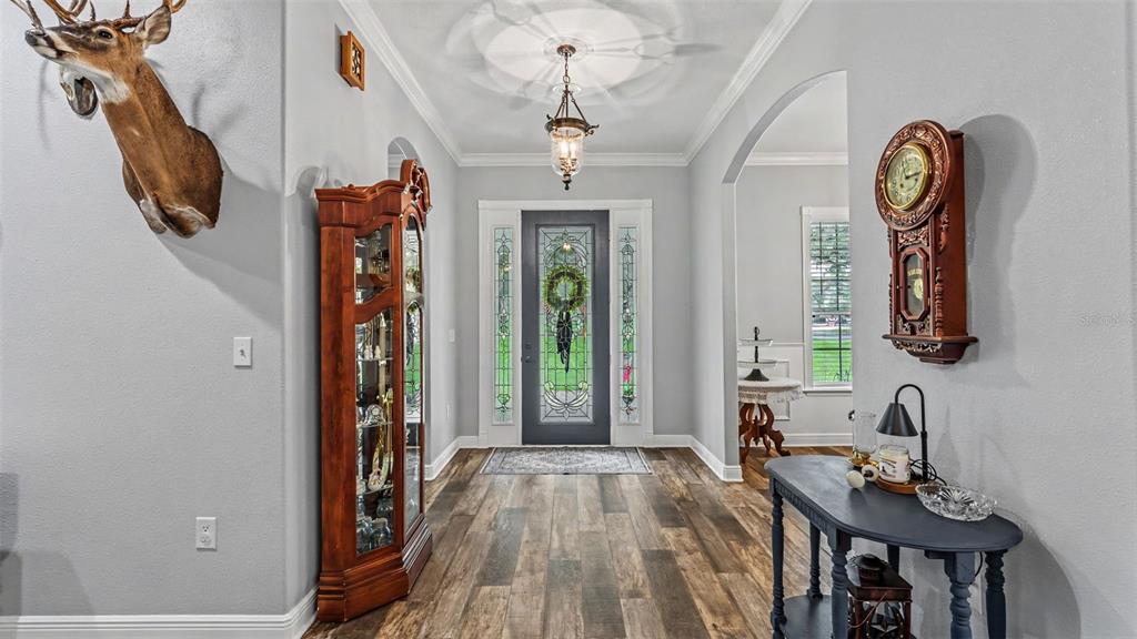 An entryway features wood-look flooring, a glass-paneled front door, a display cabinet, and wall decor — 8044 LAKE HATCHINEHA ROAD, HAINES CITY, FL