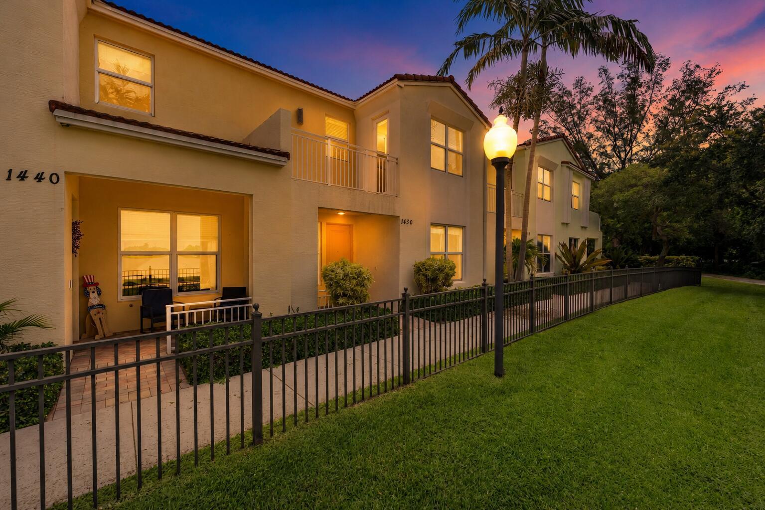 A two-story stucco townhouse with a black metal fence and a sunset sky background — 1430 NW 48th Lane, Boca Raton FL 33431, BOCA RATON, FL