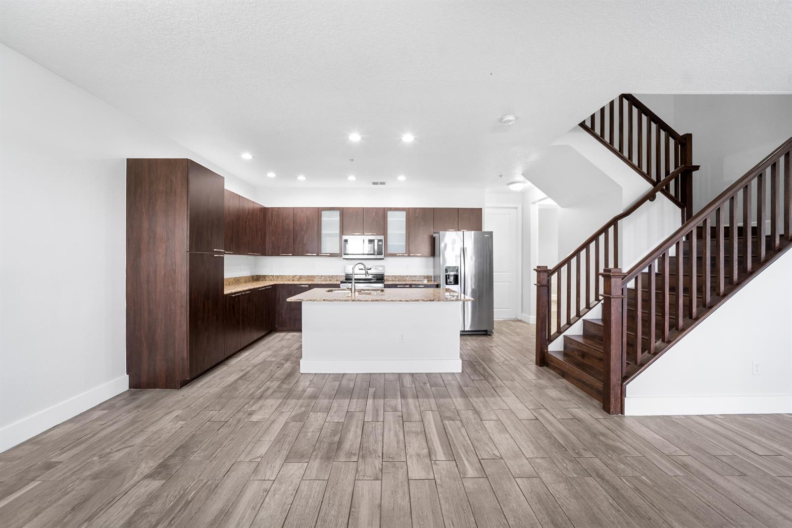 A kitchen with dark wood cabinets, granite countertops, a central island, and a wooden staircase — 1430 NW 48th Lane, Boca Raton FL 33431, BOCA RATON, FL