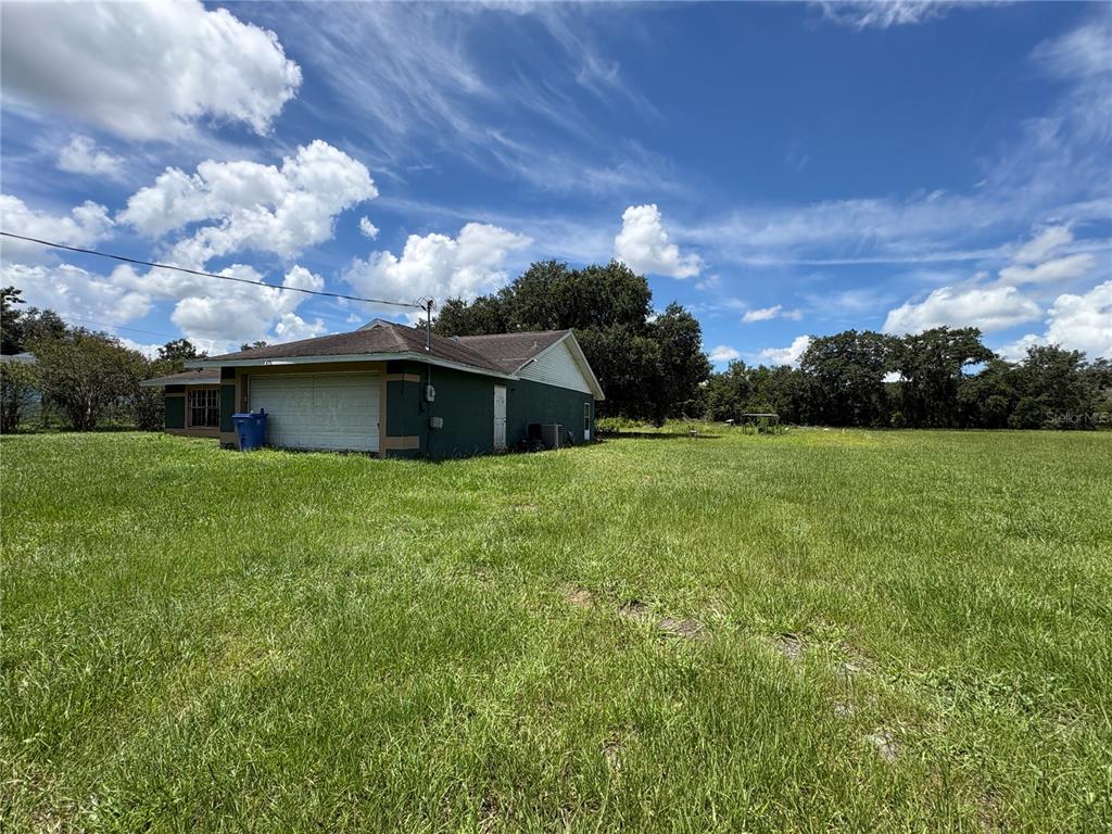 A green house with a garage sits on a large, grassy lot under a blue sky — 4951 JOHN WESLEY PLACE, PLANT CITY, FL
