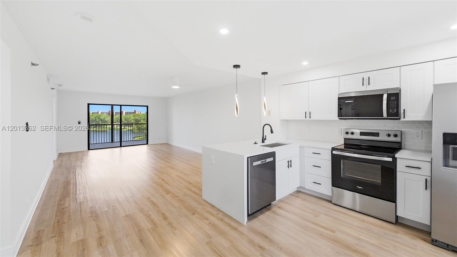 A modern kitchen with white cabinetry and stainless steel appliances opens to a living area — 2232 N Cypress Bend Dr # 507, Pompano Beach FL 33069, POMPANO BEACH, FL