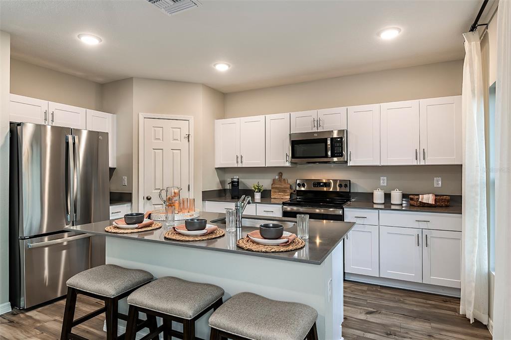 A kitchen with white cabinets, stainless steel appliances, and a gray island with bar stools — 31685 OYSTER TRELLIS LANE, WESLEY CHAPEL, FL