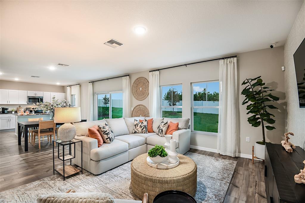 A bright living room features a sectional sofa, a round ottoman, and an open kitchen — 31685 OYSTER TRELLIS LANE, WESLEY CHAPEL, FL