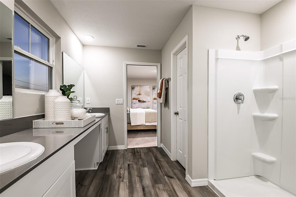 A bathroom features a double vanity with gray countertops, wood-look flooring, and a white shower — 31685 OYSTER TRELLIS LANE, WESLEY CHAPEL, FL