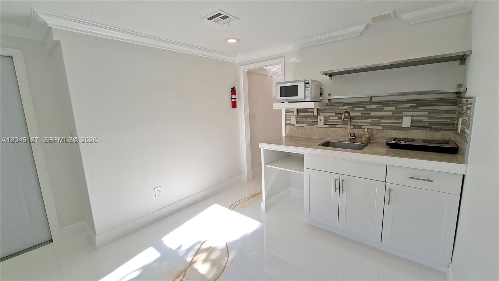 A small kitchen area features white cabinets, a sink, a microwave, and open shelving — 1028 S 62nd Ave # B, Hollywood FL 33023, HOLLYWOOD, FL