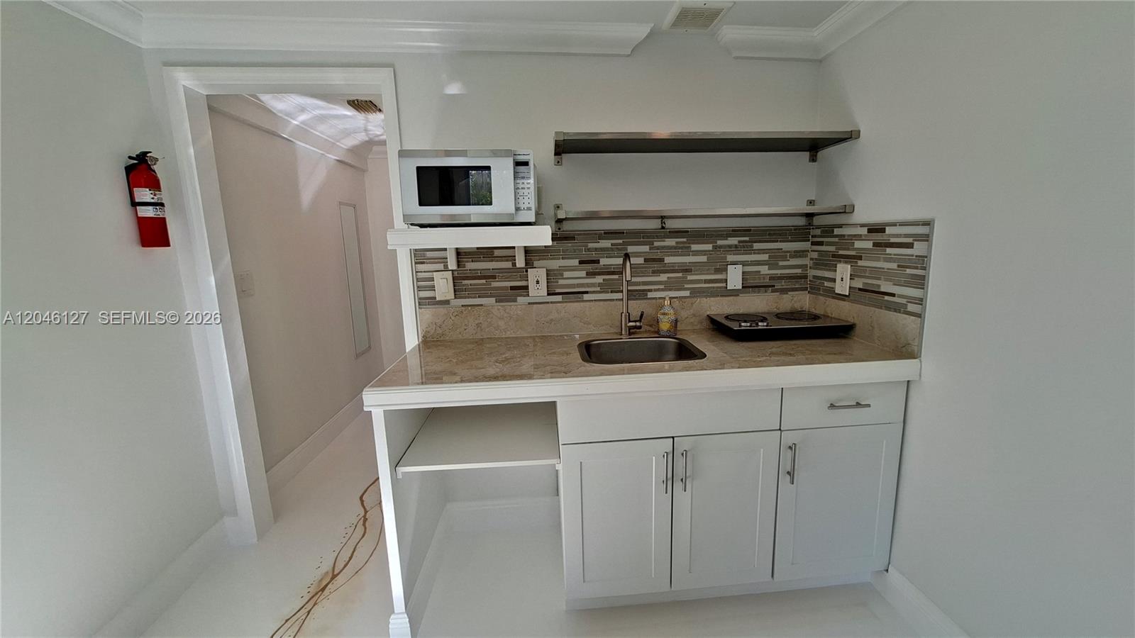 A small kitchenette features white cabinets, a sink, a microwave, and open metal shelving — 1028 S 62nd Ave # B, Hollywood FL 33023, HOLLYWOOD, FL
