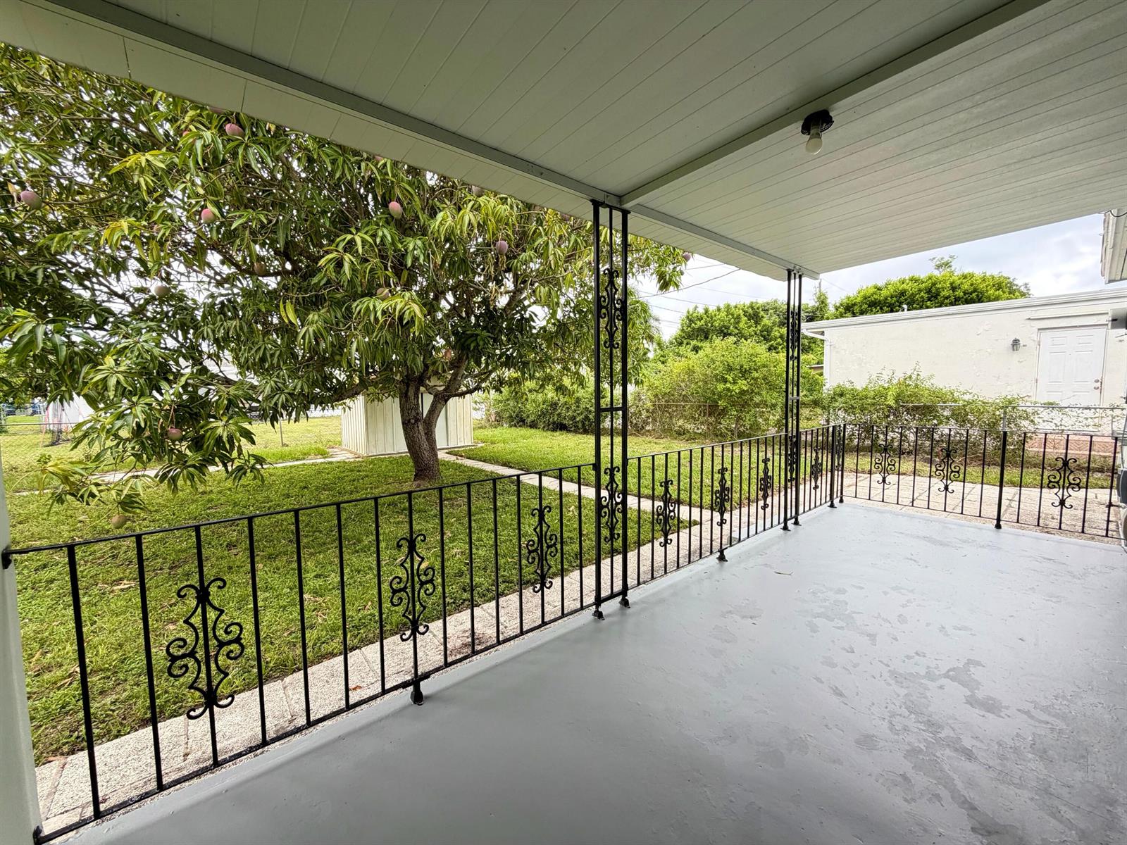 A covered porch with gray painted flooring and black decorative metal railings overlooks a backyard — 831 El Prado, West Palm Beach FL 33405, WEST PALM BEACH, FL