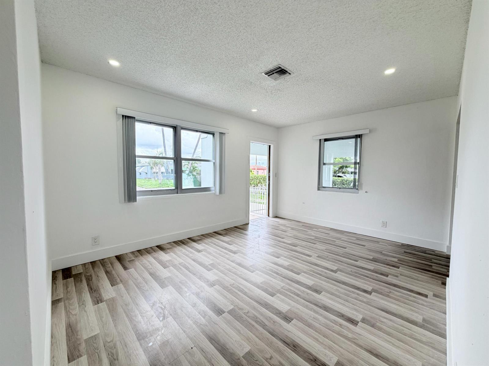 An empty room features white walls, wood-look flooring, recessed lighting, and two windows — 831 El Prado, West Palm Beach FL 33405, WEST PALM BEACH, FL