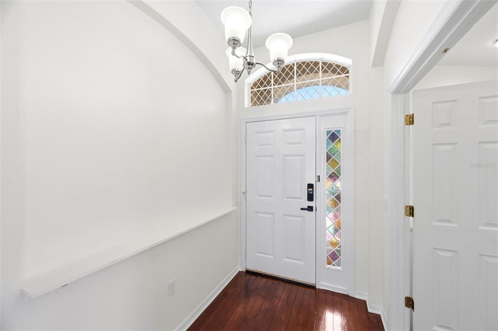 An entryway features a white front door with stained glass, a chandelier, and hardwood floors — 13510 GLOSSY IBIS PLACE, BRADENTON, FL