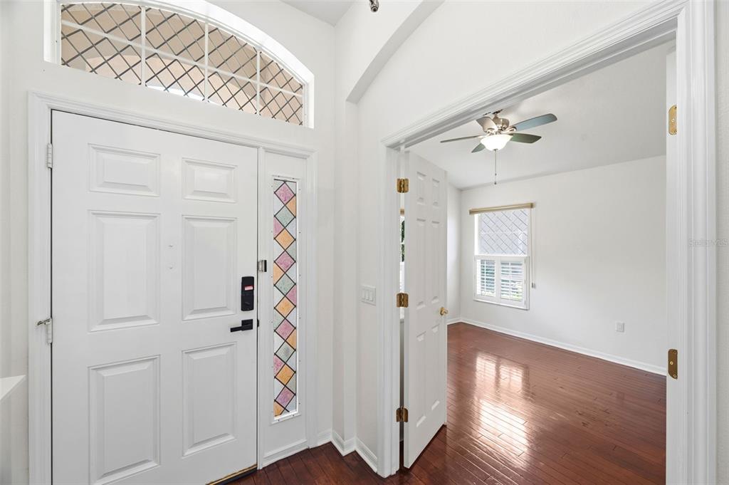An entryway with a white front door, stained glass sidelight, and an adjacent room with wood floors — 13510 GLOSSY IBIS PLACE, BRADENTON, FL
