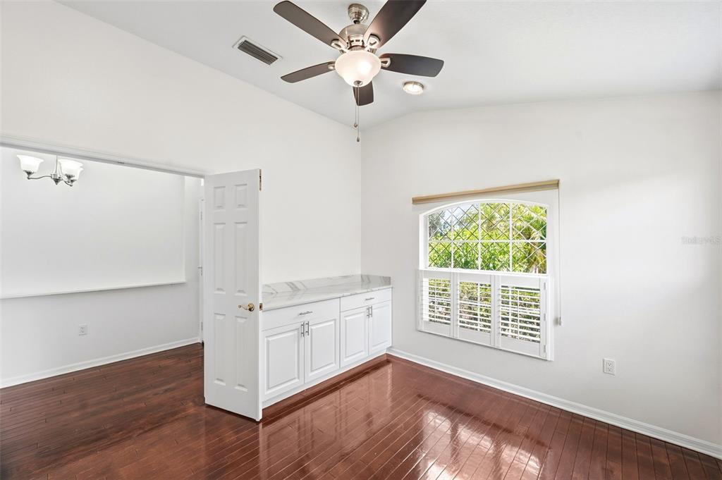 A room with dark wood floors, white cabinets, a ceiling fan, and a window with shutters — 13510 GLOSSY IBIS PLACE, BRADENTON, FL
