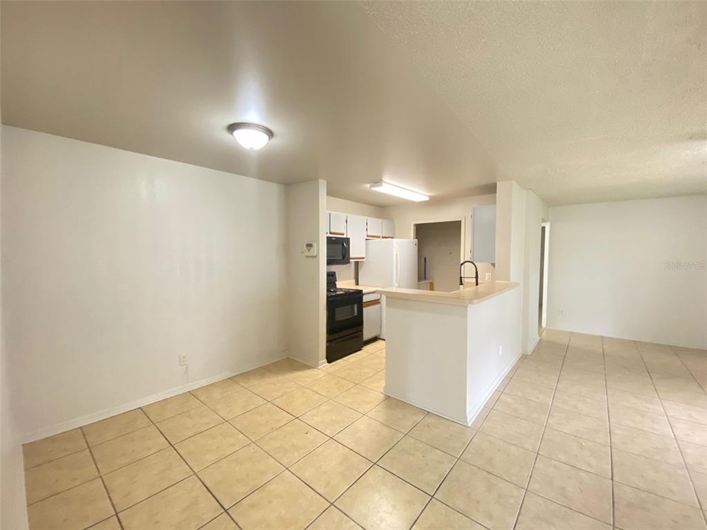 A kitchen with white cabinets, black appliances, and a breakfast bar overlooks a tiled dining area — 6100 WESTGATE DRIVE UNIT 103, ORLANDO, FL