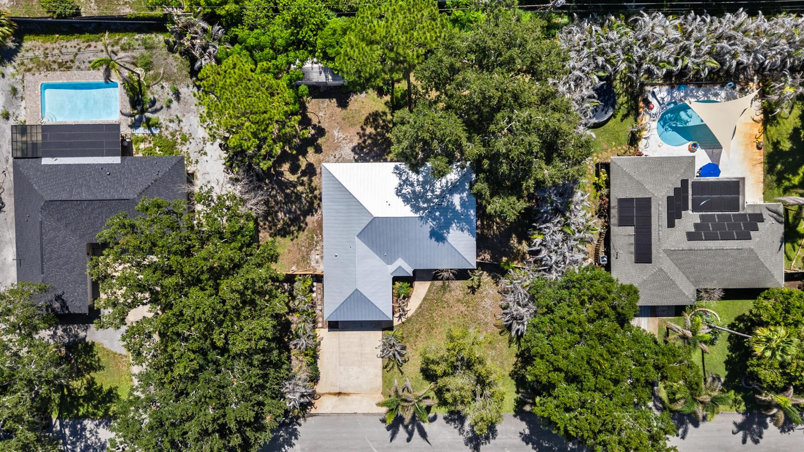 An aerial view shows three houses with pools, surrounded by trees and paved driveways — VERO BEACH, FL