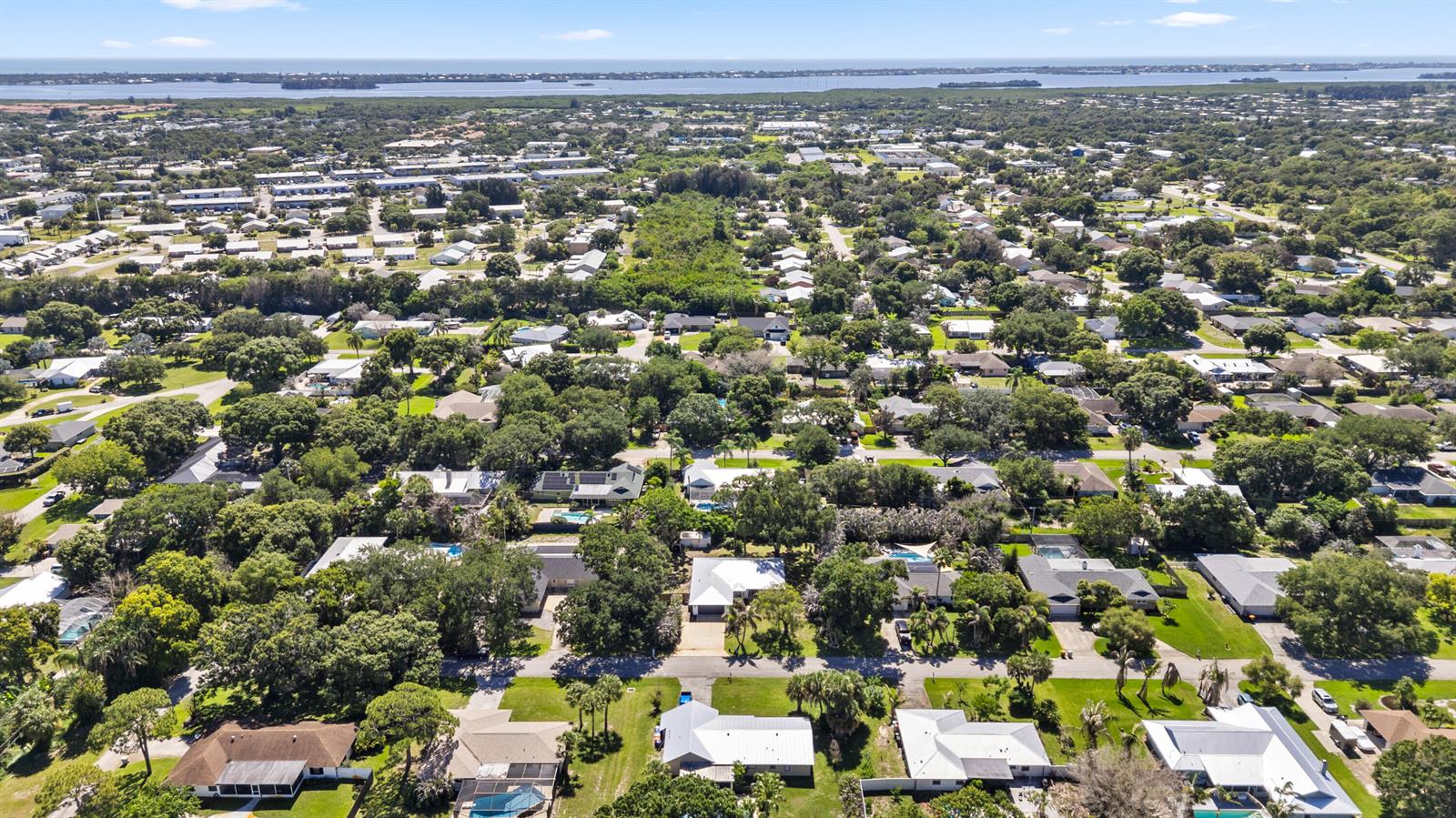 An aerial view shows a suburban neighborhood with many trees and houses near a bay — VERO BEACH, FL