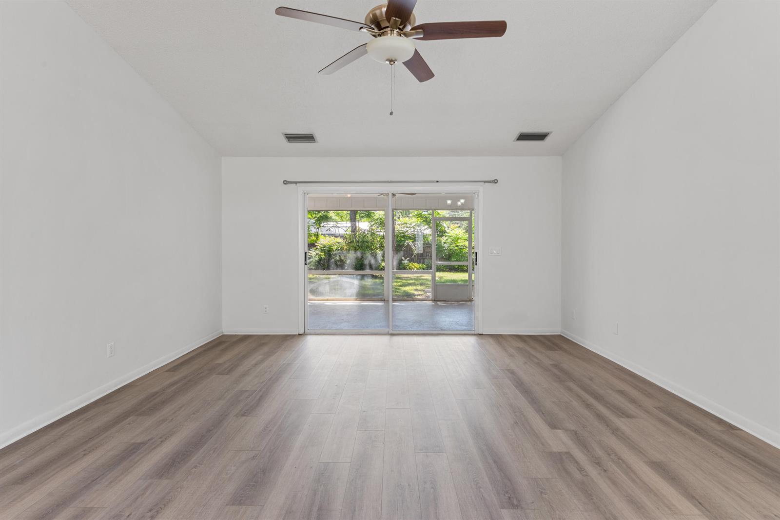 An empty room features light wood-look flooring, white walls, a ceiling fan, and sliding glass doors — VERO BEACH, FL