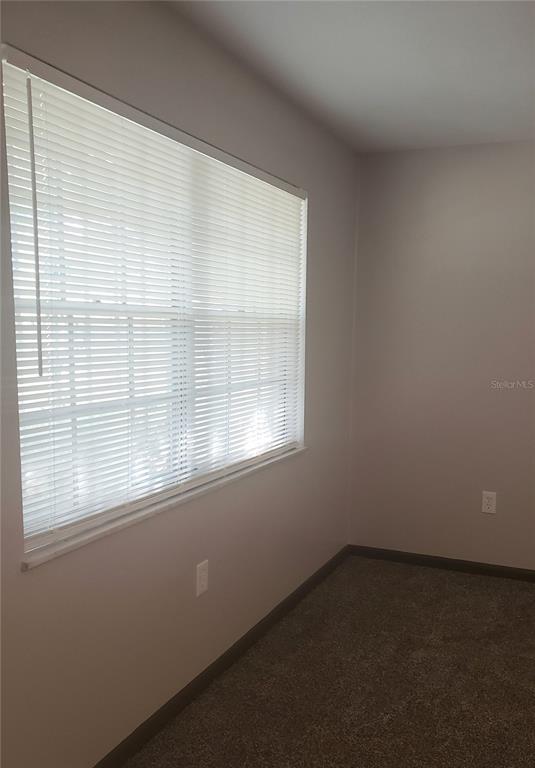 A bedroom with beige walls, carpeted flooring, and a window covered by white horizontal blinds — 5652 18TH STREET, ZEPHYRHILLS, FL