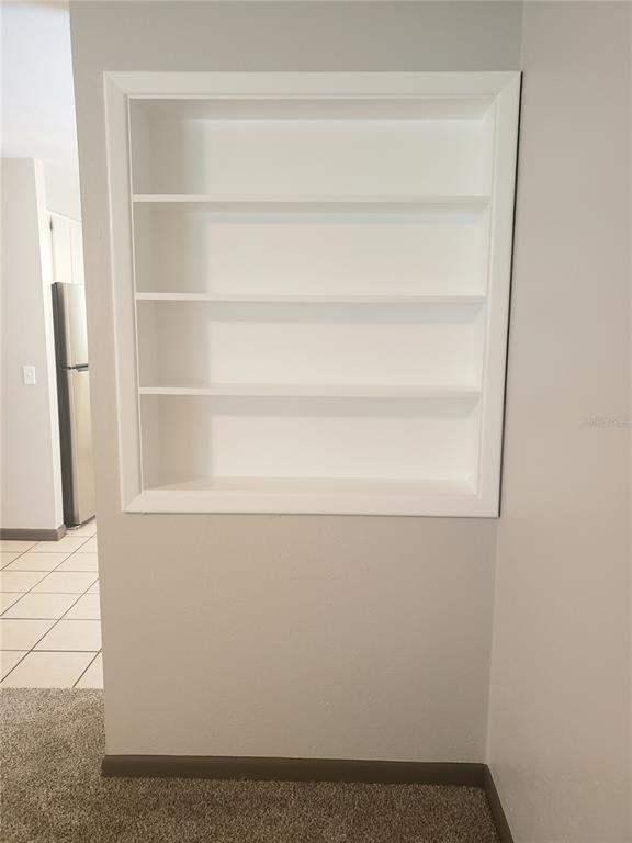 A wall-mounted white recessed shelving unit with four shelves sits above a carpeted floor — 5652 18TH STREET, ZEPHYRHILLS, FL