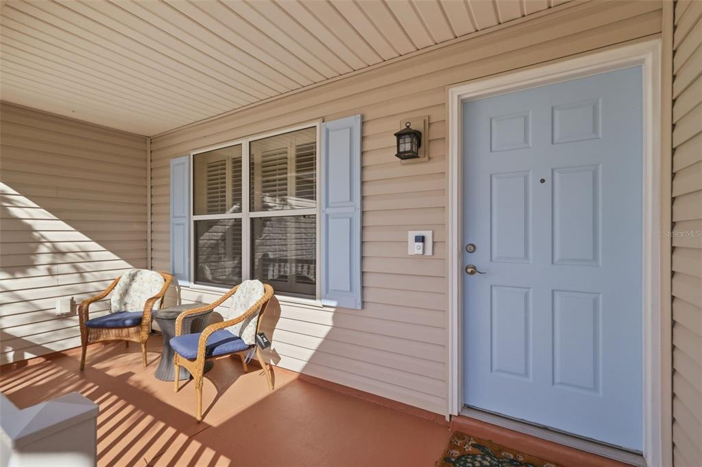 A covered porch features light-colored siding, a light blue front door, and two wicker chairs — 1609 BLOSSOM TERRACE, THE VILLAGES, FL