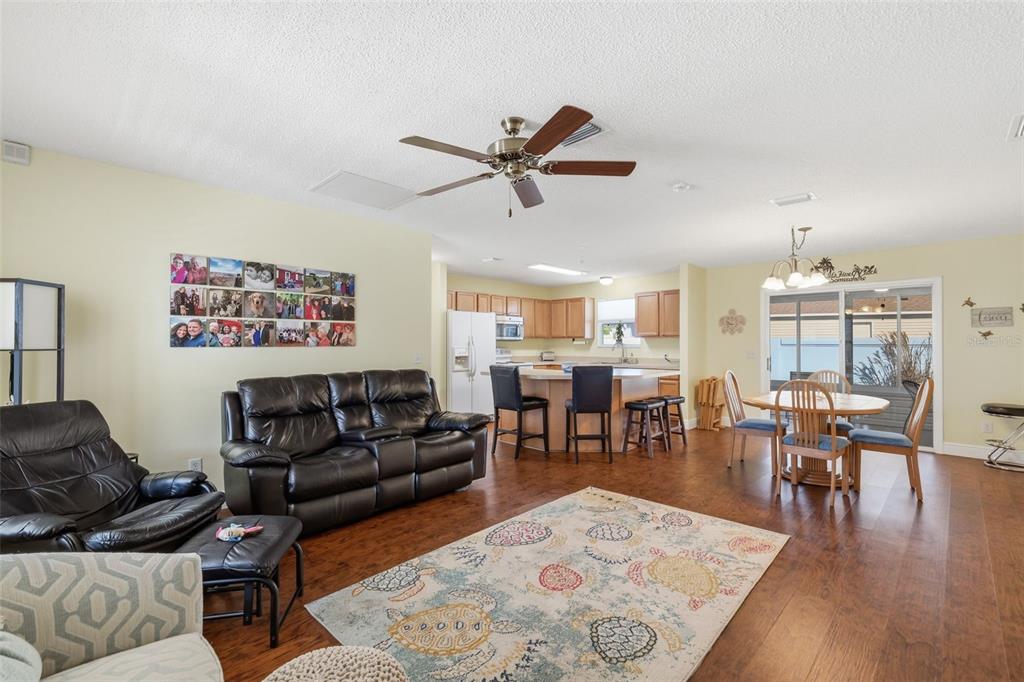 An open-concept living and dining area with wood flooring, a ceiling fan, and kitchen island — 1609 BLOSSOM TERRACE, THE VILLAGES, FL