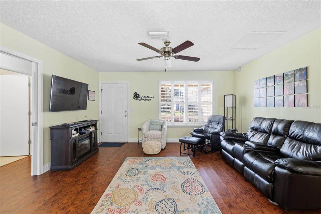 A living room features wood flooring, a ceiling fan, a television, and a leather sofa — 1609 BLOSSOM TERRACE, THE VILLAGES, FL