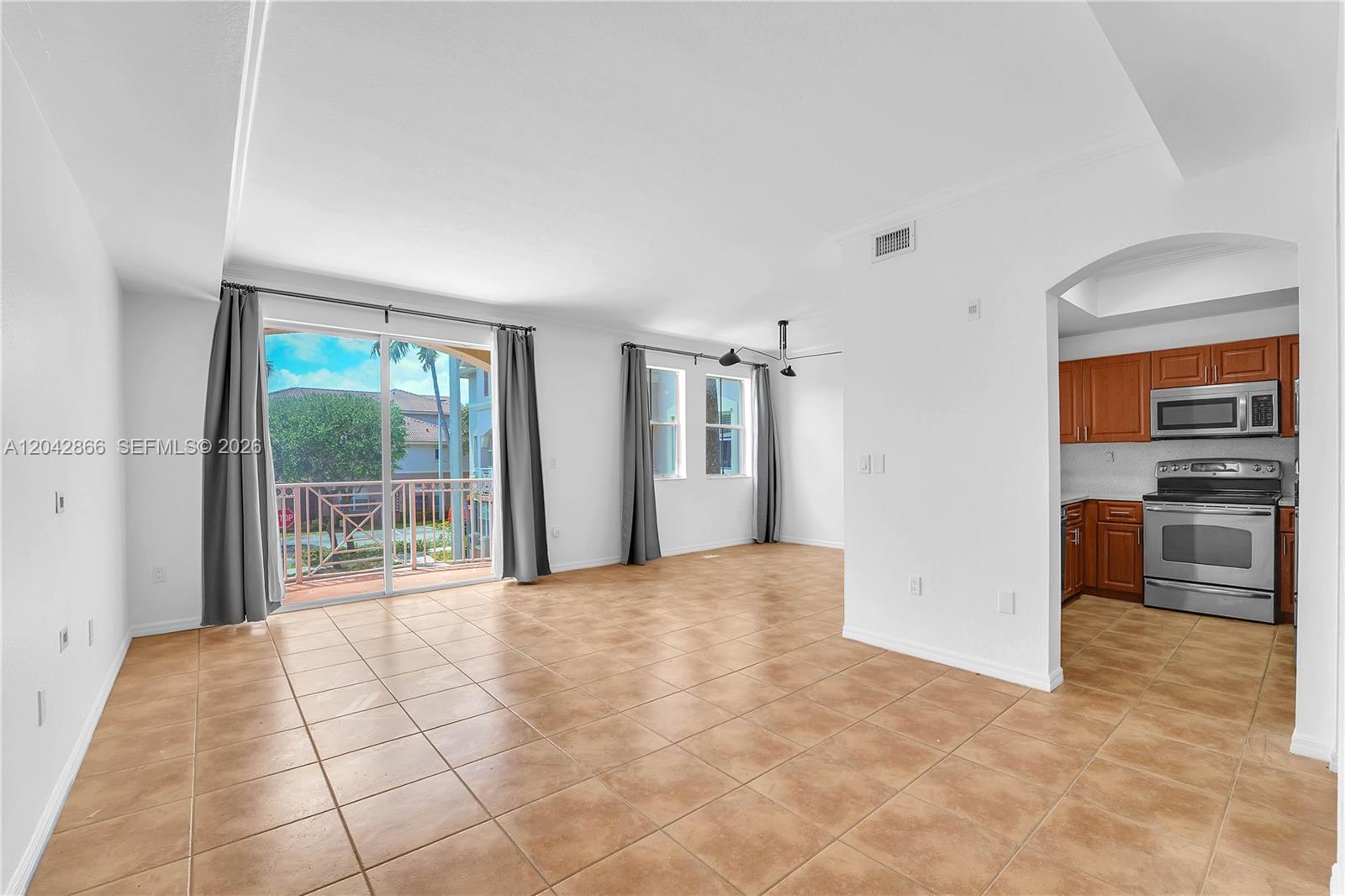 A tiled hallway leads to a living area with a balcony and sliding glass doors — 8858 W Flagler St # 210, Miami FL 33174, MIAMI, FL