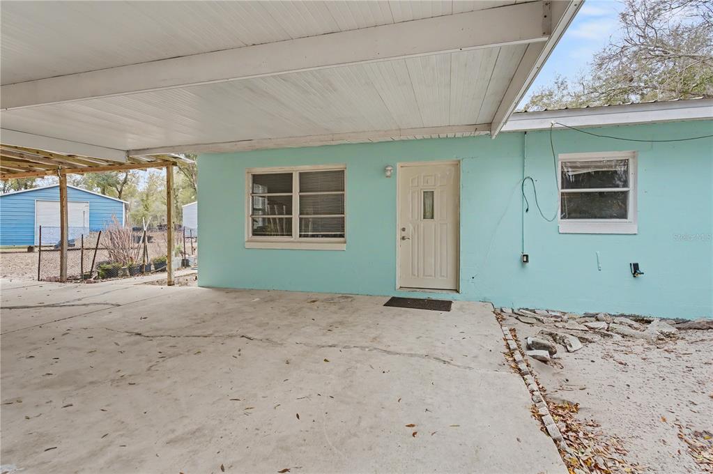 A turquoise exterior wall features a white door and window under a covered carport — 5710 NE 140TH COURT, WILLISTON, FL