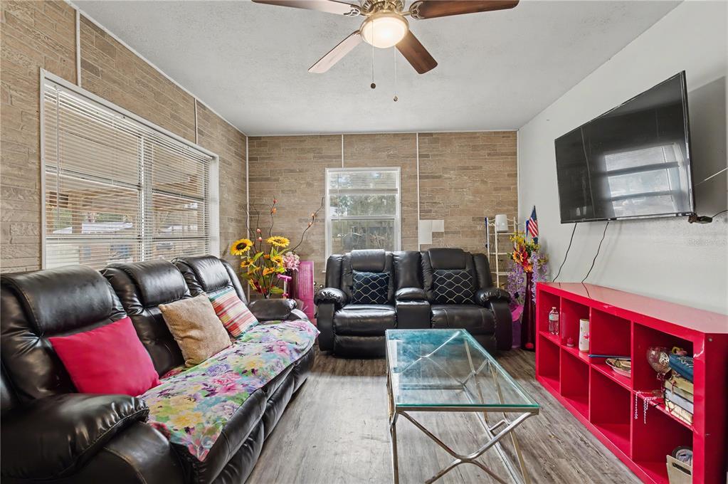 A living room features stone-textured walls, a ceiling fan, black leather furniture, and red shelving — 5710 NE 140TH COURT, WILLISTON, FL