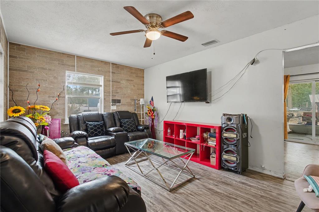 A living room features a wood-look accent wall, a red shelving unit, and leather furniture — 5710 NE 140TH COURT, WILLISTON, FL