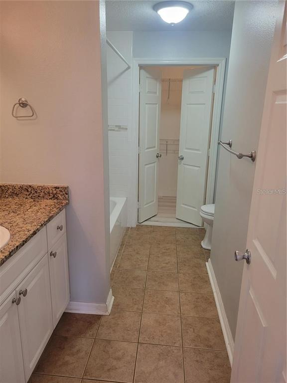 A bathroom with a granite vanity, tile flooring, a bathtub, and an open walk-in closet — 501 KNIGHTS RUN AVENUE UNIT 1113, TAMPA, FL