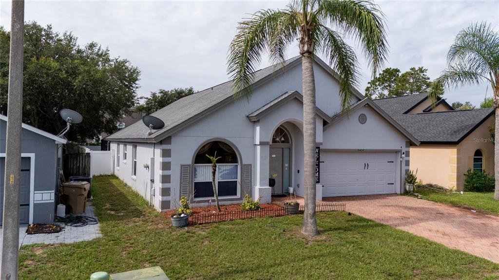 A single-story house with a white stucco exterior, a palm tree, and a brick driveway — 16404 COOPERS HAWK AVENUE, CLERMONT, FL