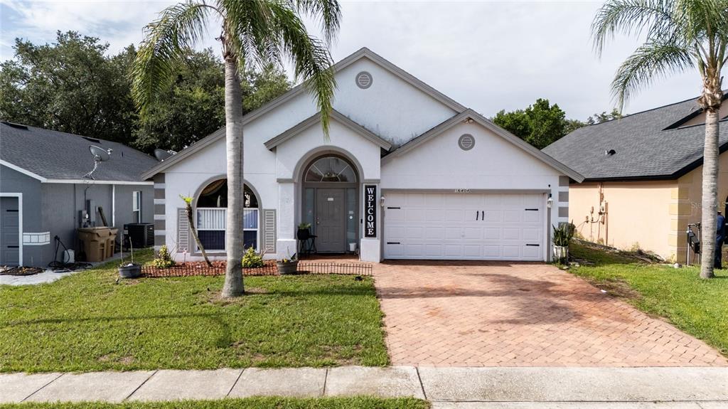 A single-story house with a white stucco exterior, a brick driveway, and two palm trees — 16404 COOPERS HAWK AVENUE, CLERMONT, FL