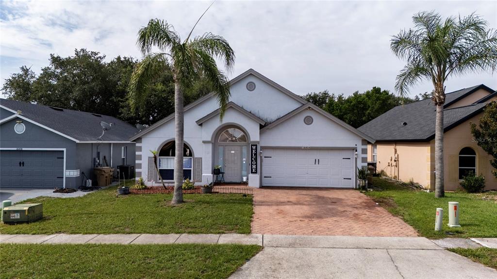 A single-story house with a white stucco facade, a two-car garage, and two palm trees — 16404 COOPERS HAWK AVENUE, CLERMONT, FL