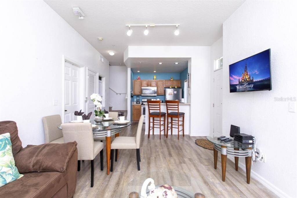 A living room with a dining area and kitchen featuring wood cabinets and bar stools — 2201 SAN VITTORINO CIRCLE UNIT 108, KISSIMMEE, FL