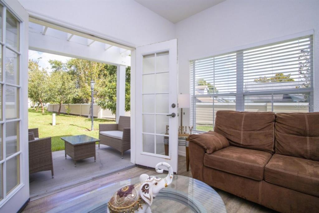A sunroom with a brown sofa, glass coffee table, and open doors leading to a patio — 2201 SAN VITTORINO CIRCLE UNIT 108, KISSIMMEE, FL