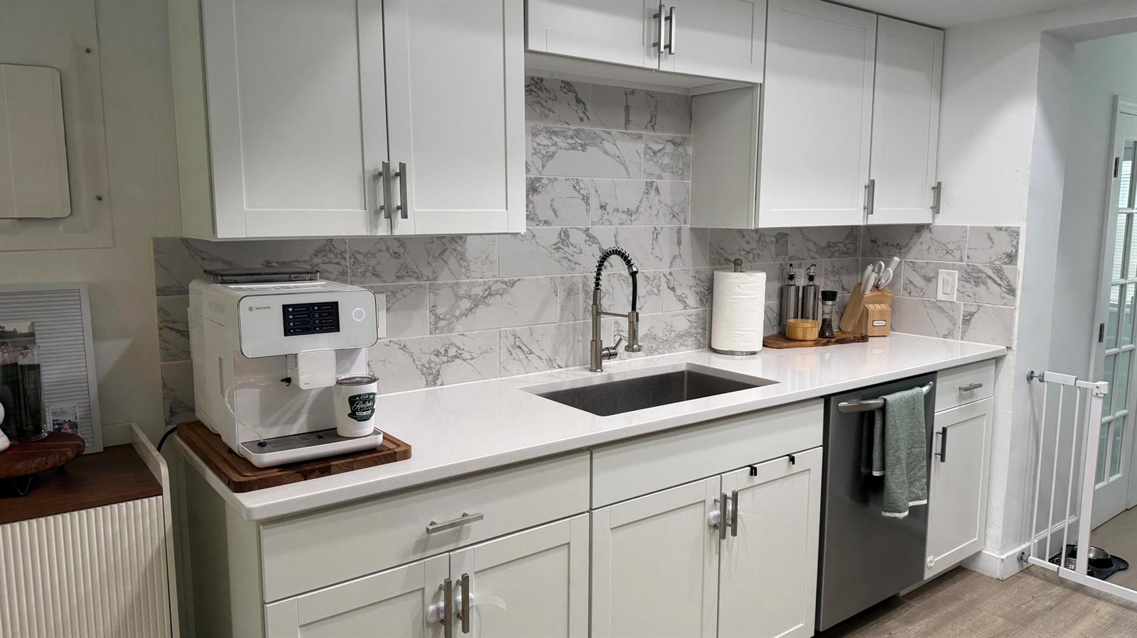 A kitchen with white cabinets, stainless steel appliances, marble-look backsplash, and light wood-look flooring — 125 Doe Trail, Jupiter FL 33458, JUPITER, FL