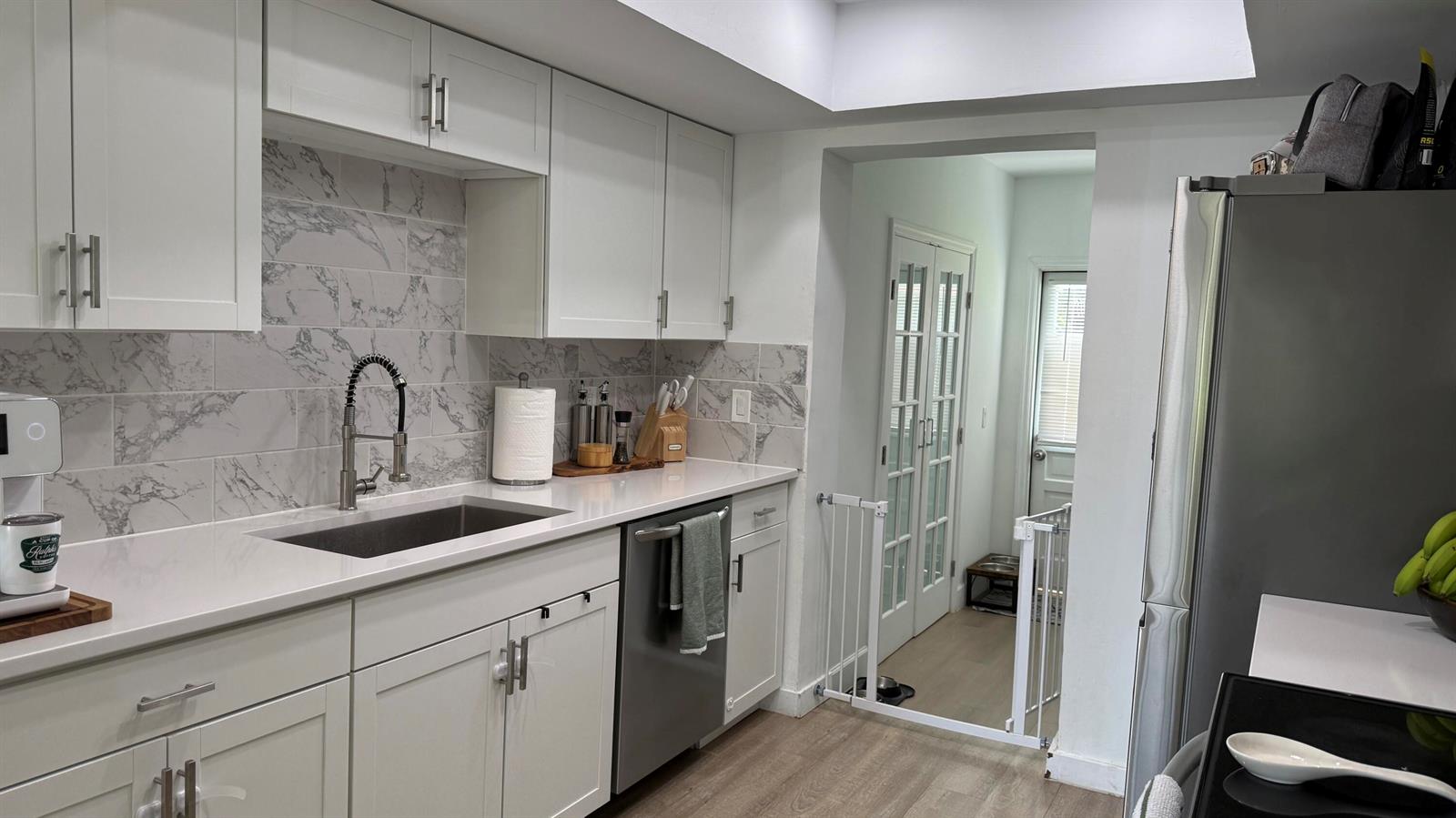 A white kitchen with marble-look backsplash, stainless steel appliances, and a doorway leading outside — 125 Doe Trail, Jupiter FL 33458, JUPITER, FL