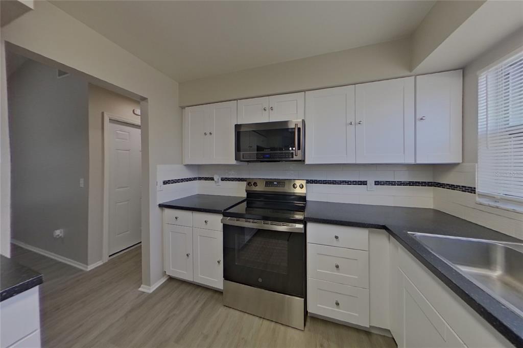 A kitchen with white cabinets, black countertops, stainless steel appliances, and a tiled backsplash — 39 TROTTERS CIRCLE, KISSIMMEE, FL