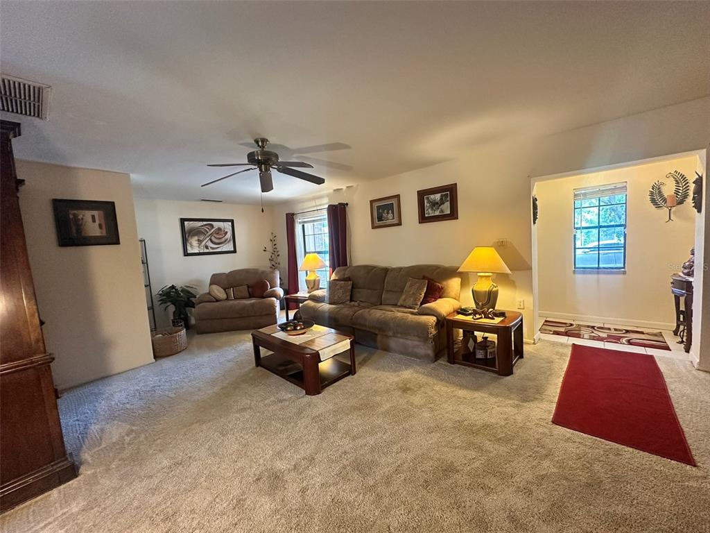 A living room with beige carpet, a brown sofa, a coffee table, and a ceiling fan — 5626 STULL AVENUE, ORLANDO, FL