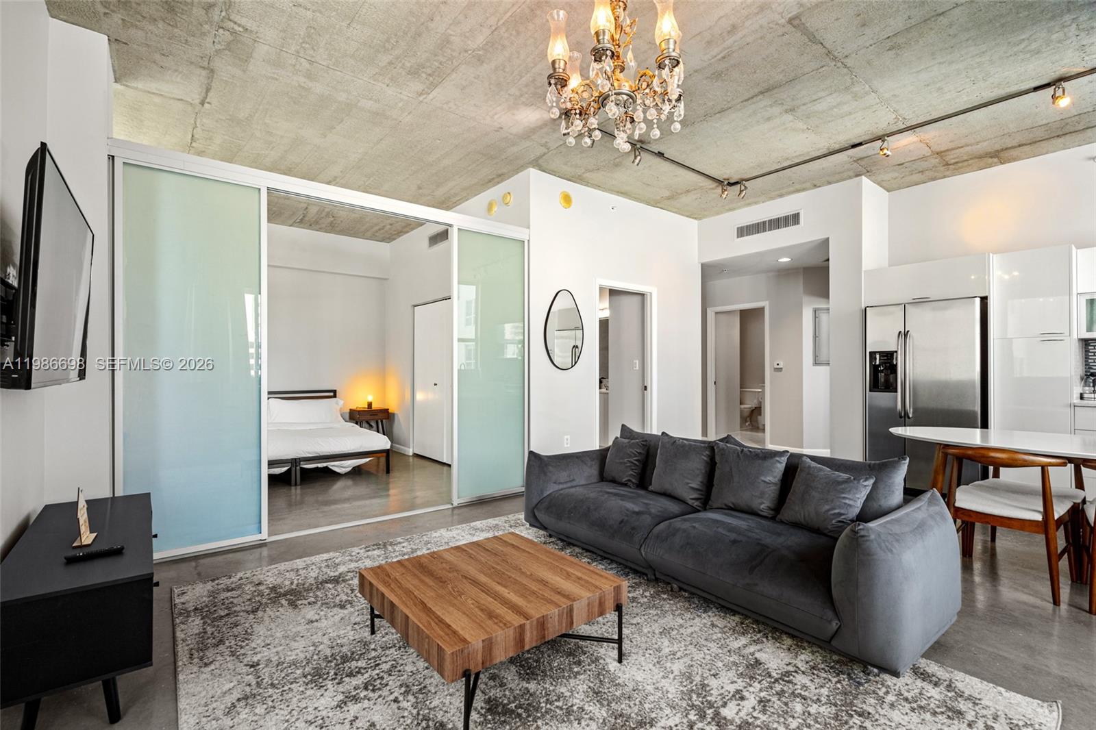 A living room with a concrete ceiling, grey sofa, and sliding glass bedroom doors — 133 NE 2nd Ave # 912, Miami FL 33132, MIAMI, FL