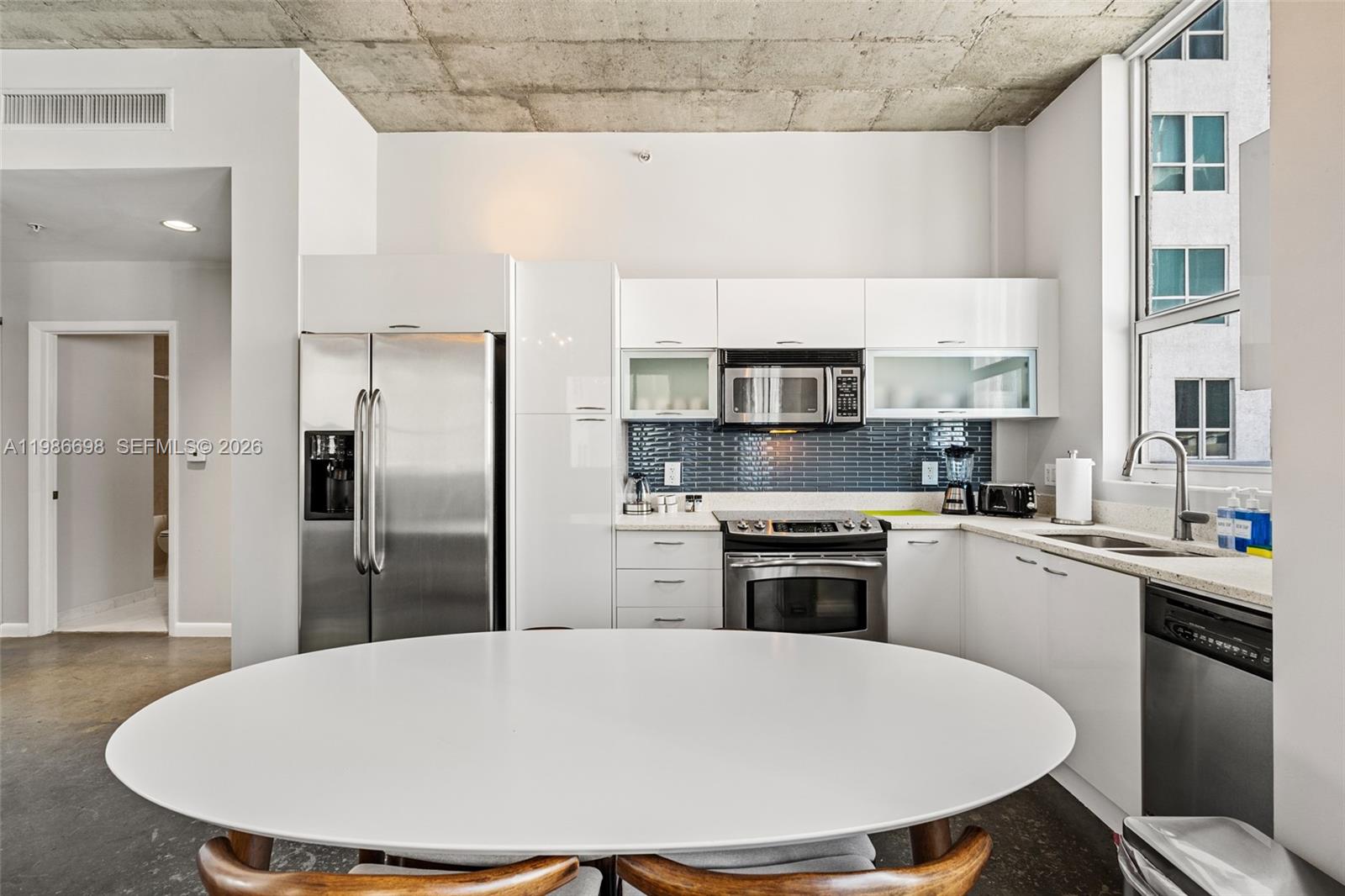 A modern kitchen features white cabinets, stainless steel appliances, and a concrete ceiling — 133 NE 2nd Ave # 912, Miami FL 33132, MIAMI, FL