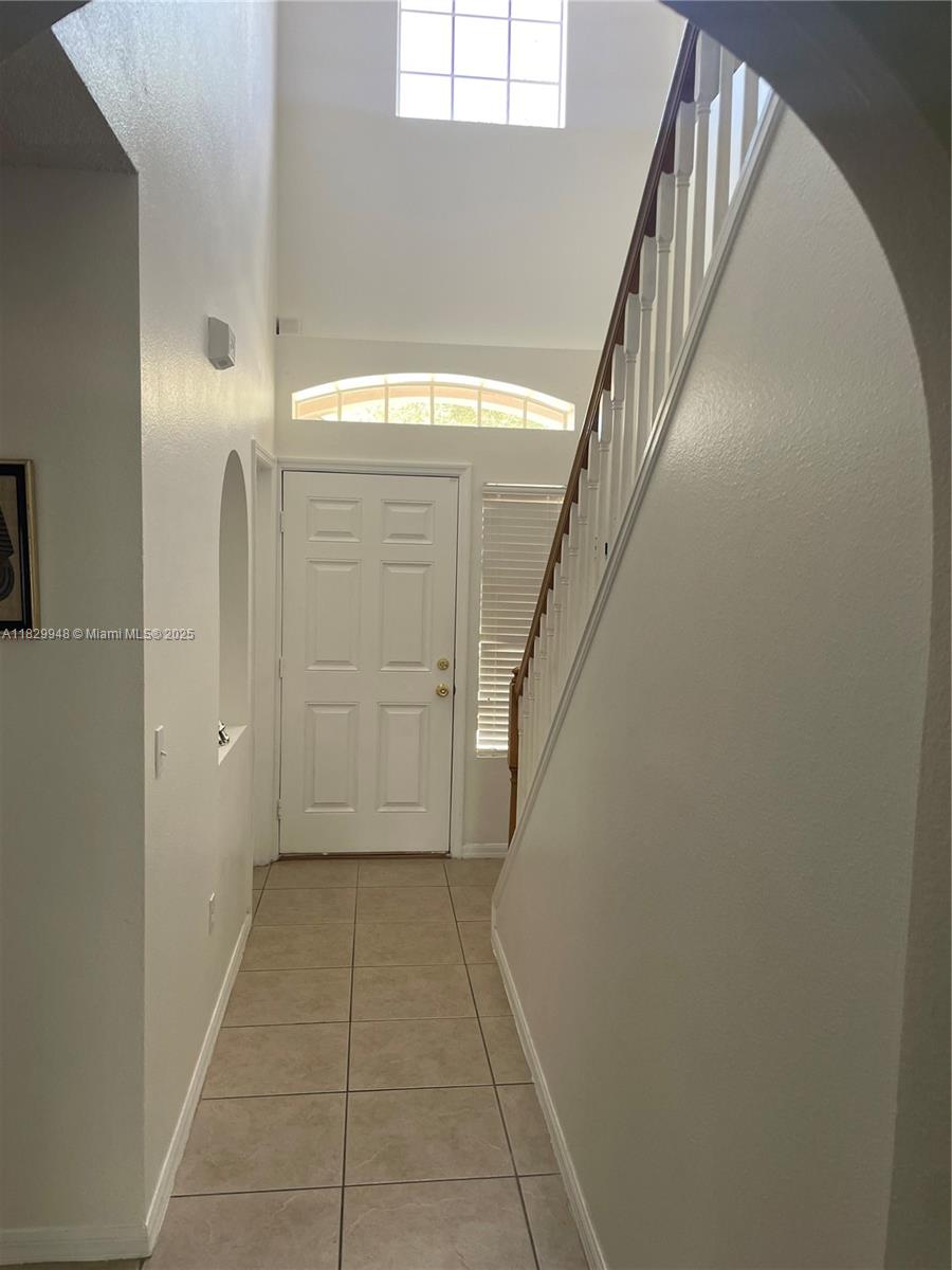 A tiled entryway features a staircase with a wooden railing and a high ceiling — 2645 SW 12th Sq SW, Vero Beach FL 32968, VERO BEACH, FL