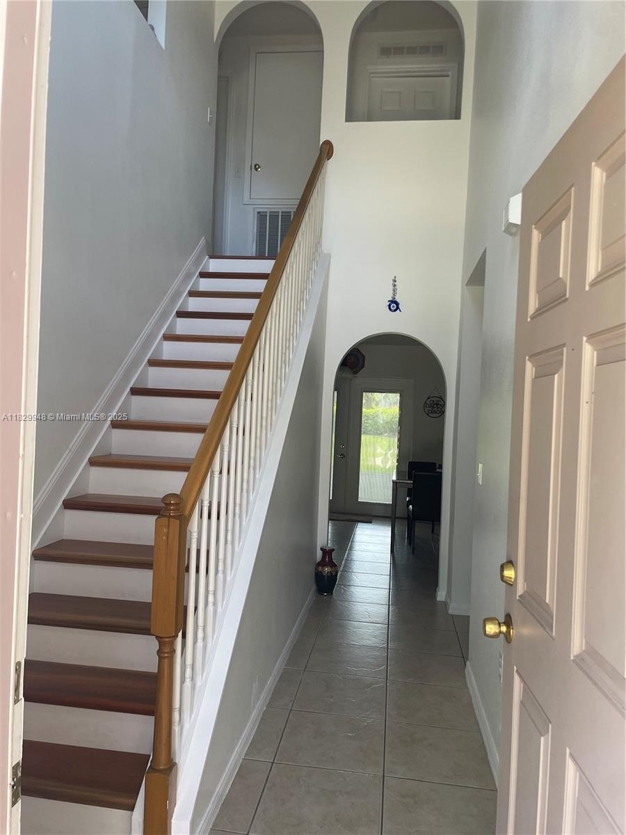 An entryway features a tiled floor, a wooden staircase with white railings, and arched doorways — 2645 SW 12th Sq SW, Vero Beach FL 32968, VERO BEACH, FL