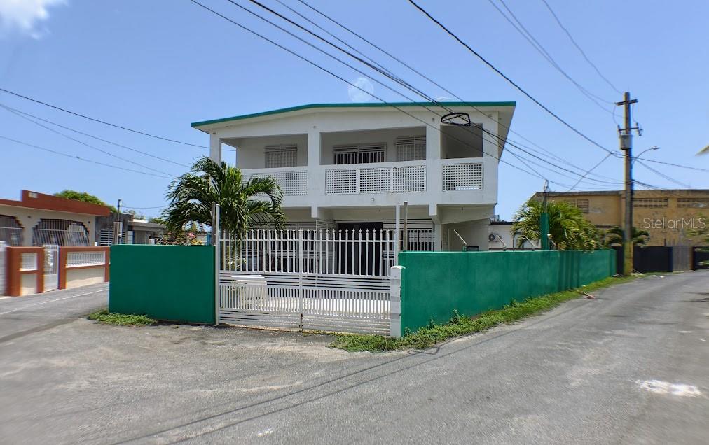 A two-story white house with a green perimeter wall and a gated driveway — PR-187 VILLA KENNEDY COMMUNITY LOT 149, LOIZA, PR