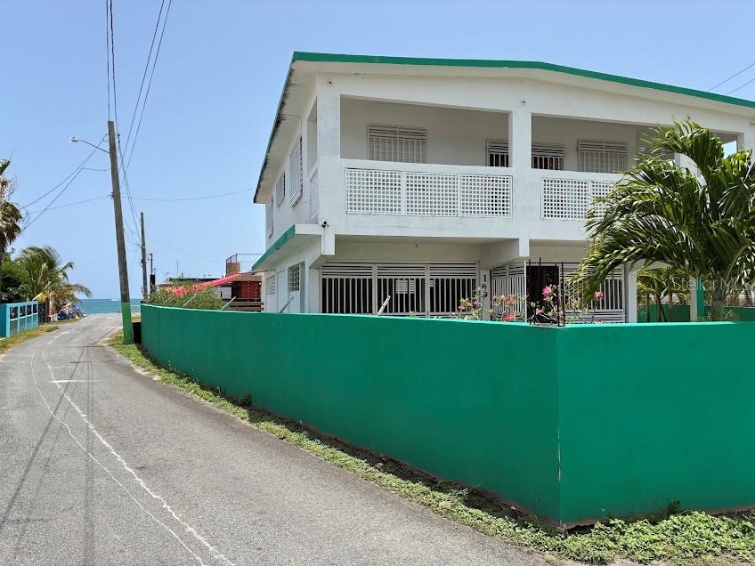 A two-story white house with a green perimeter wall sits along a coastal road — PR-187 VILLA KENNEDY COMMUNITY LOT 149, LOIZA, PR