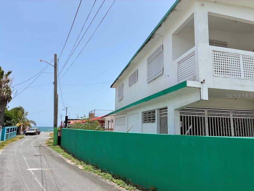 A two-story white building with a green wall stands beside a road near the ocean — PR-187 VILLA KENNEDY COMMUNITY LOT 149, LOIZA, PR