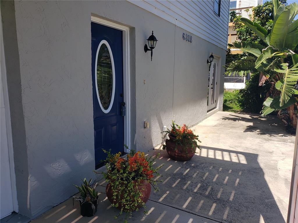 A blue front door with an oval window sits on a concrete patio with potted plants — 6318 TURTLEMOUND ROAD, NEW SMYRNA BEACH, FL