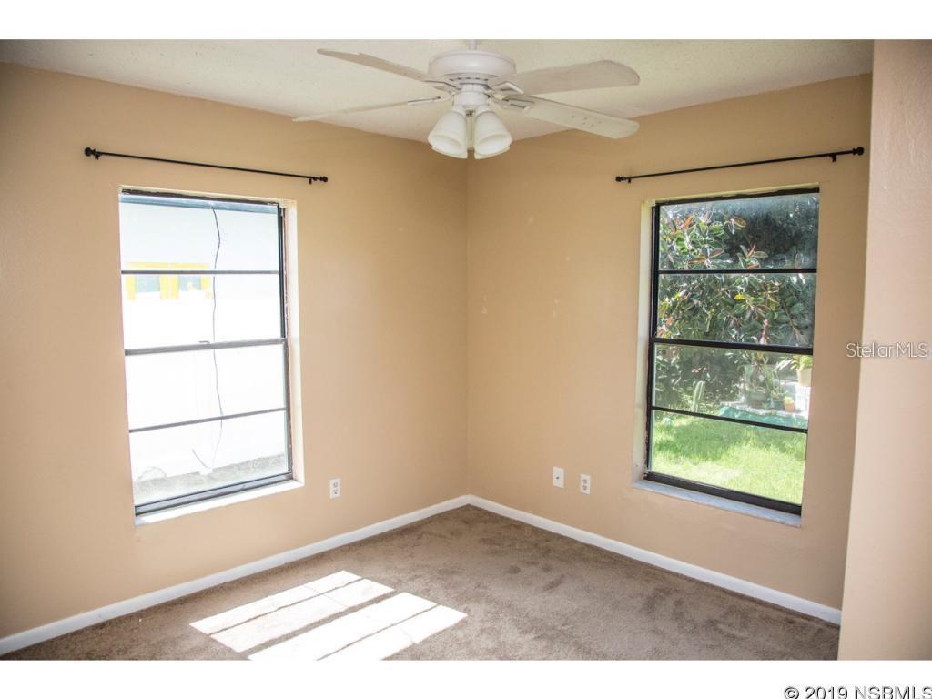 An empty bedroom features beige walls, brown carpeting, a ceiling fan, and two windows — 6318 TURTLEMOUND ROAD, NEW SMYRNA BEACH, FL