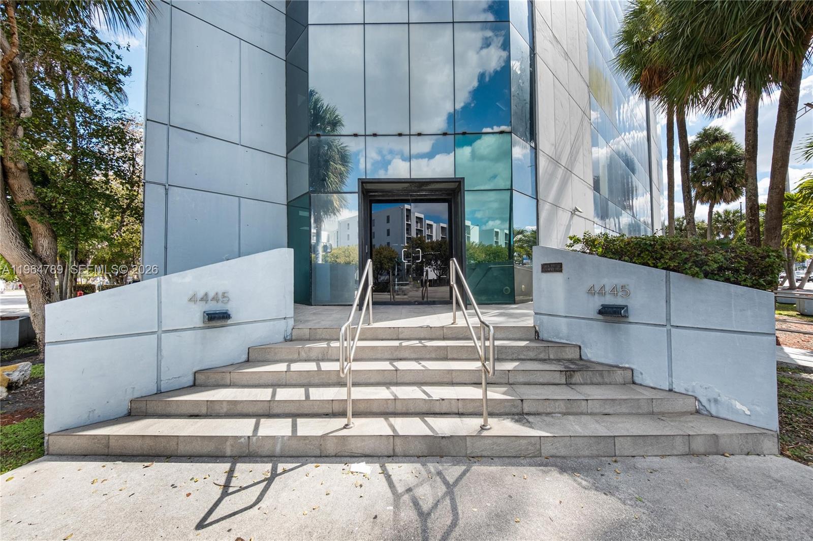 The exterior of a modern office building features a glass entrance with concrete stairs — 4445 W 16th Ave # 600, Hialeah FL 33012, HIALEAH, FL